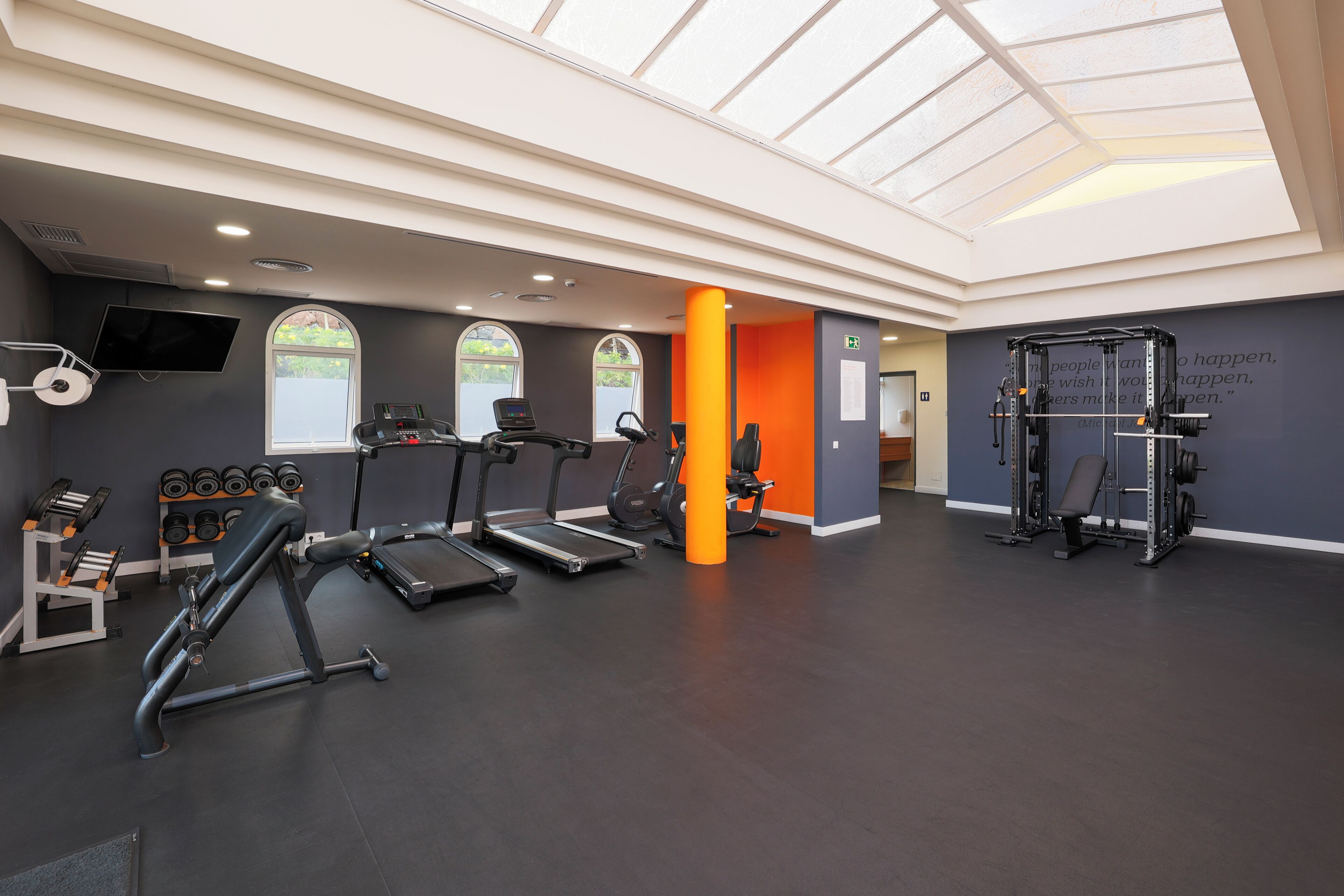 Un gimnasio con cintas de correr, un banco de pesas, mancuernas y una jaula para sentadillas.