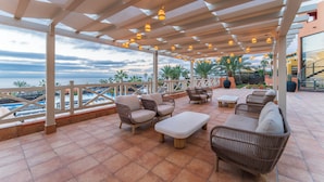 An outdoor patio with wicker furniture, a pool, and a view of the ocean. - Occidental Jandía Playa (Pajara)