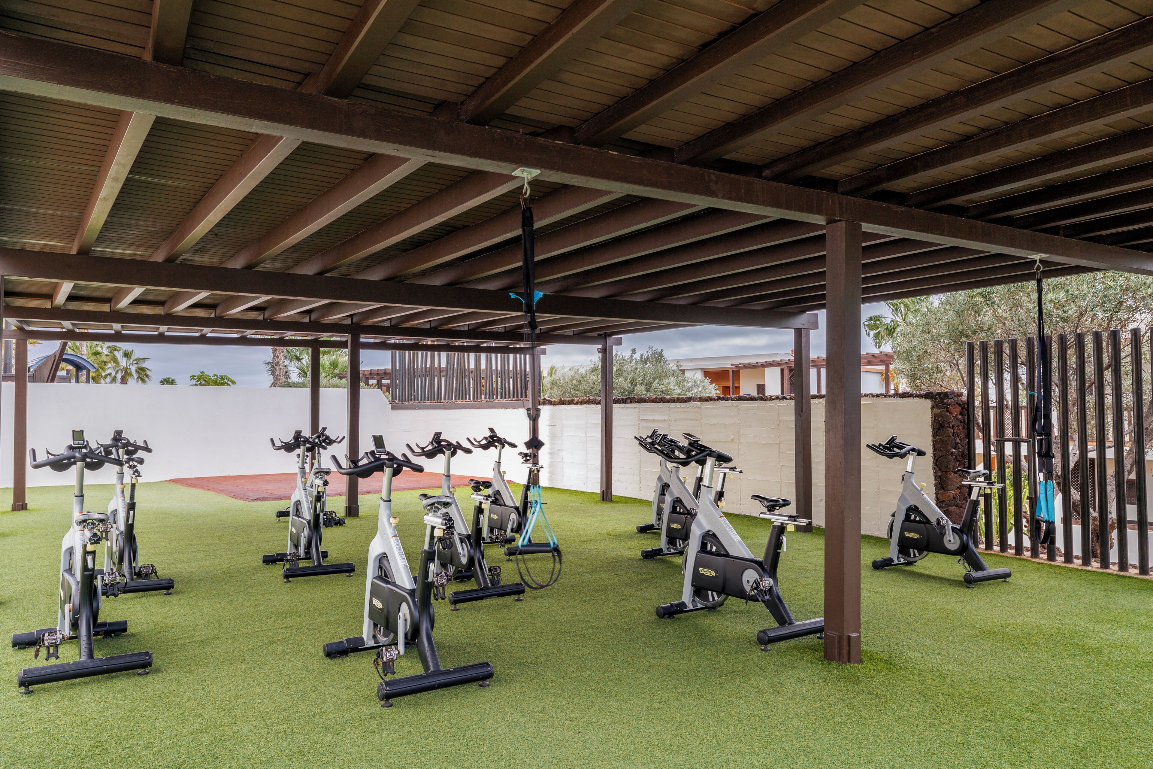 A covered outdoor gym area with stationary bikes and a tennis court.