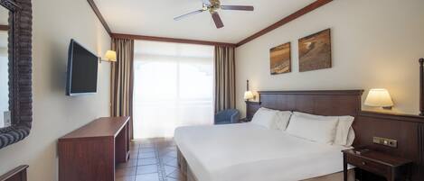 Hotelkamer met een groot bed, een plafondventilator, een flatscreen televisie, een bureau en een stoel.