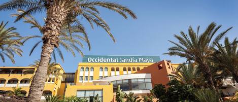 A hotel with a yellow facade, palm trees, and a clear blue sky.