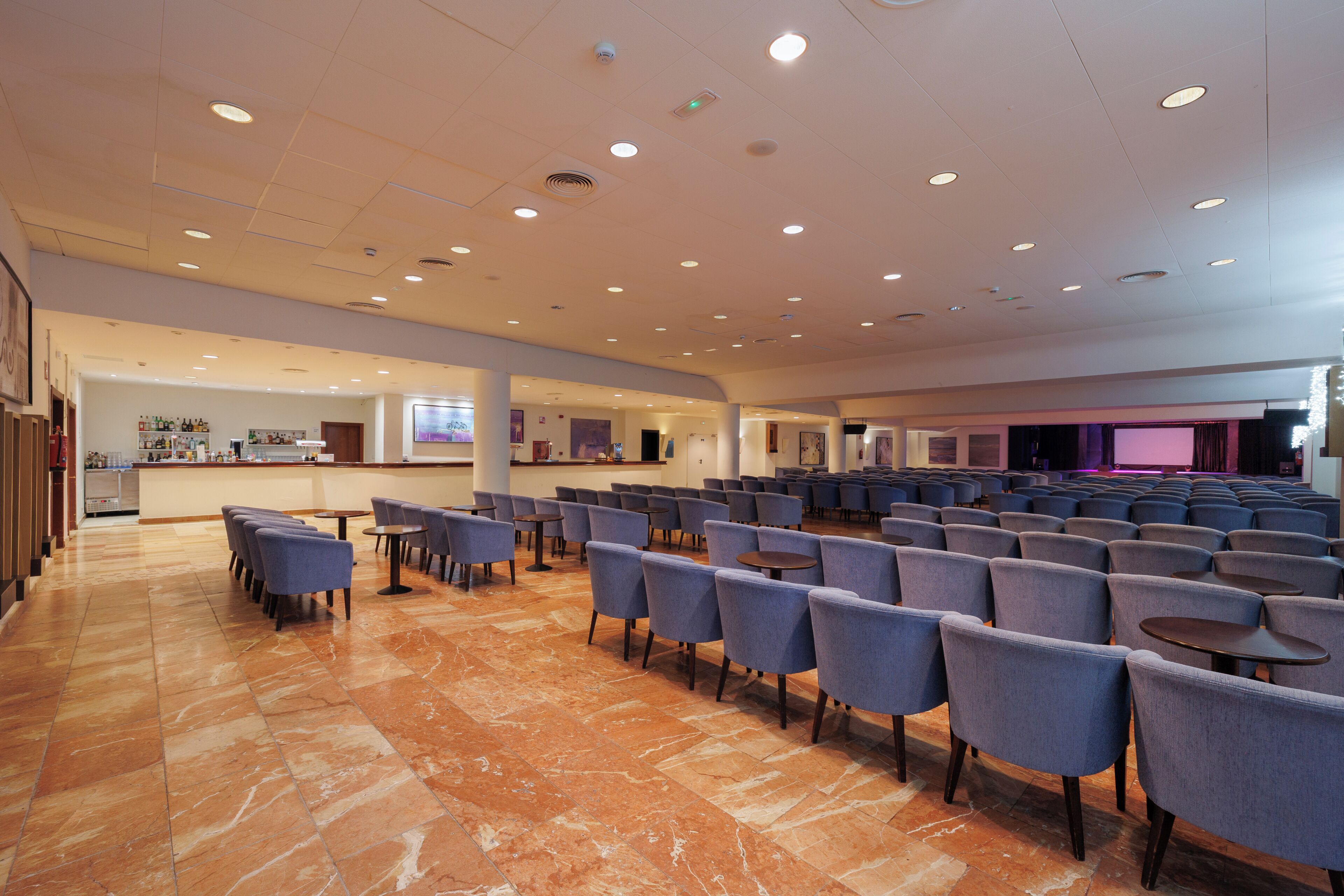 A spacious indoor area with rows of chairs and tables, a bar area, and a stage with lighting.
