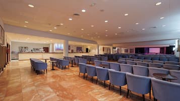 A spacious indoor area with rows of chairs and tables, a bar area, and a stage with lighting.