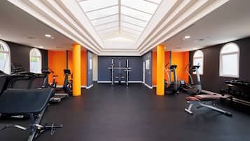 Un gimnasio con equipamiento de ejercicio, tragaluces y detalles en naranja.