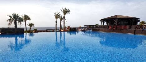 A large, clear blue pool with palm trees and a wooden deck area.