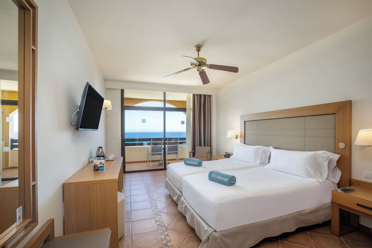A hotel room with a bed, a television, a desk, and a balcony with a view.