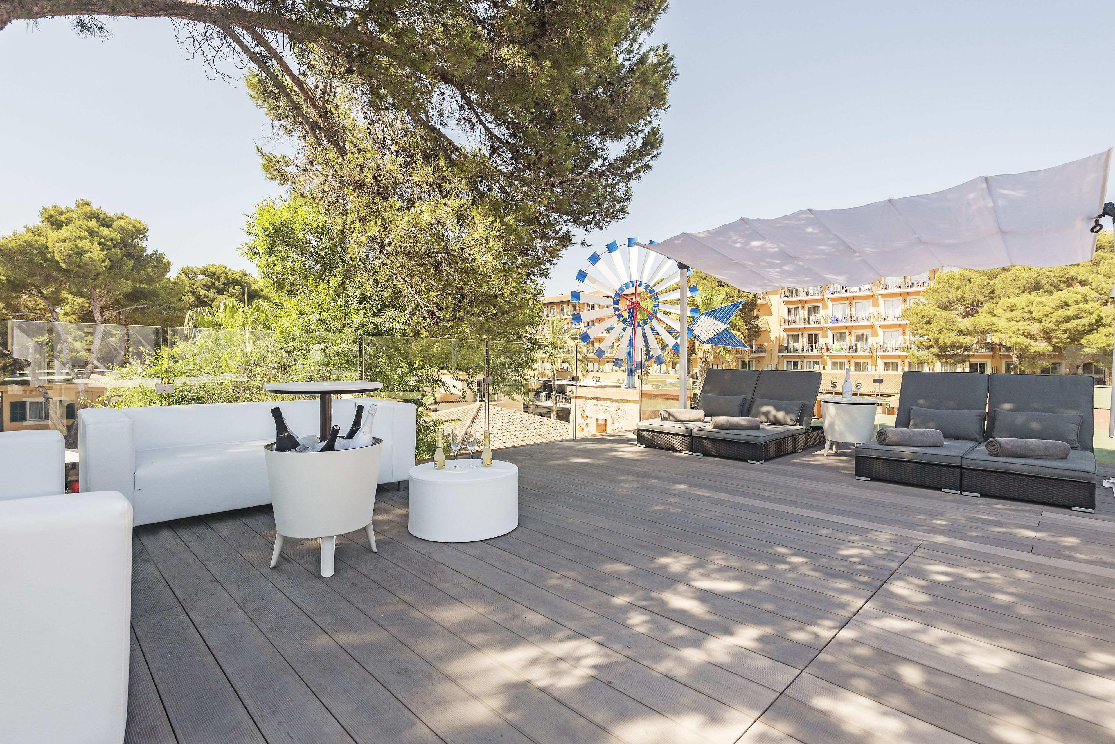 Eine Holzterrasse mit Sitzgelegenheiten im Freien, darunter Sofas und ein Tisch, und ein Riesenrad im Hintergrund.