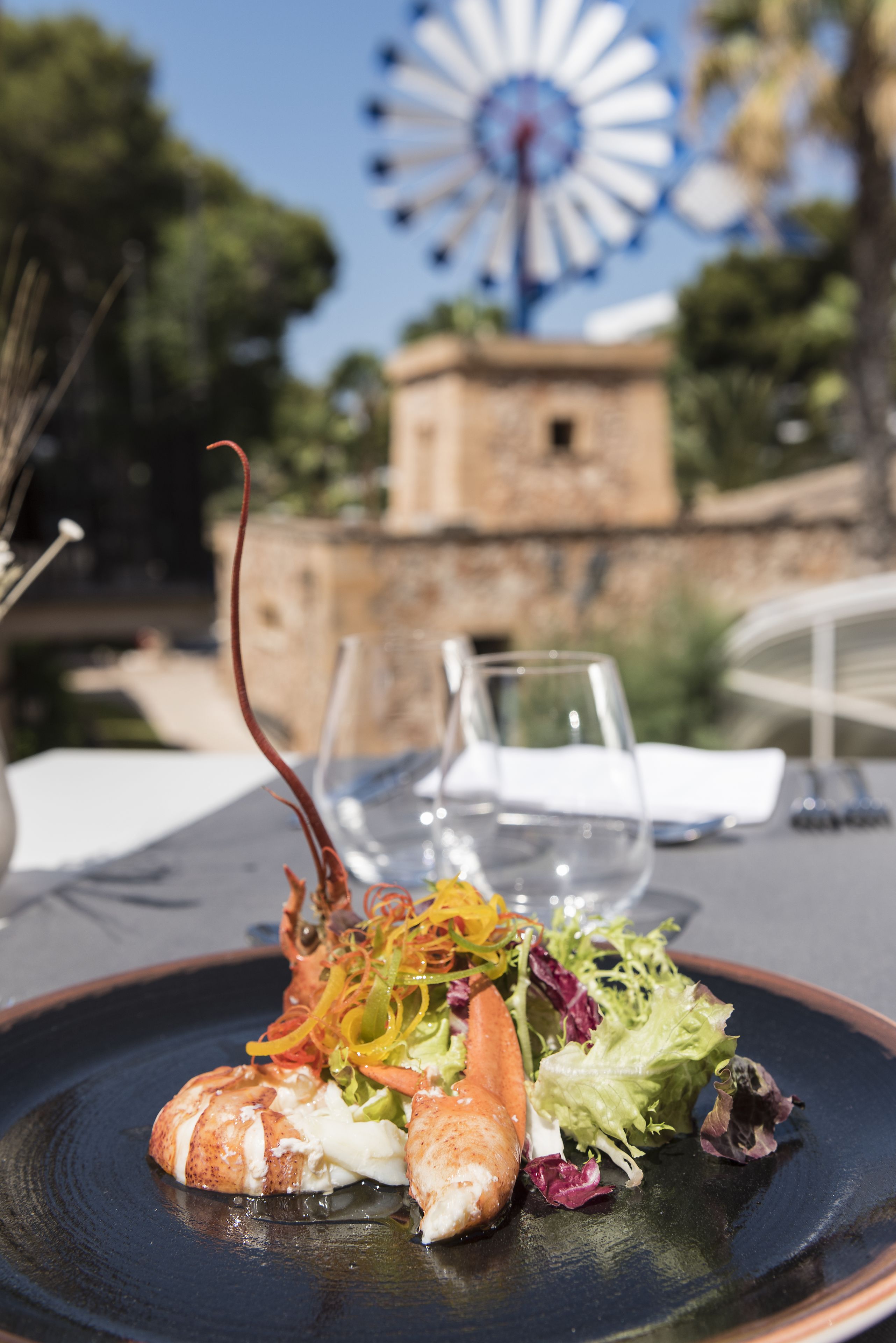 A dining table with a lobster dish, wine glasses, and a windmill in the background.