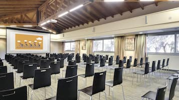 A conference room with rows of black chairs, a projector screen, and large windows with curtains.