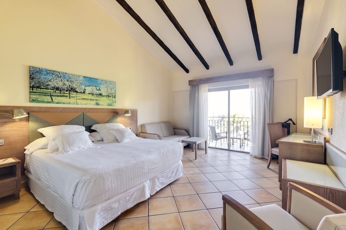 A hotel room with a large bed, a desk, a chair, and a balcony with a view.