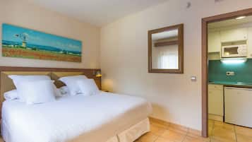 A hotel room with a large bed, a painting of a windmill, a mirror, and a kitchenette.