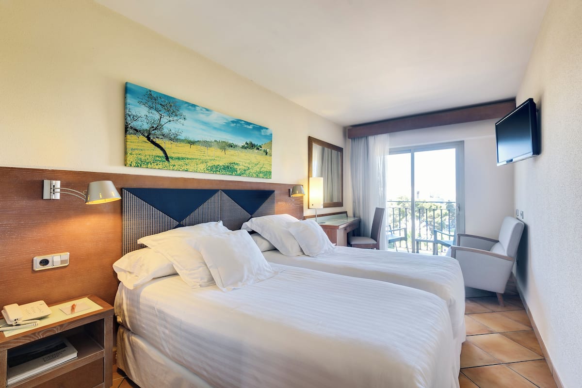 A hotel room with two beds, a desk, a chair, a TV, and a painting on the wall.