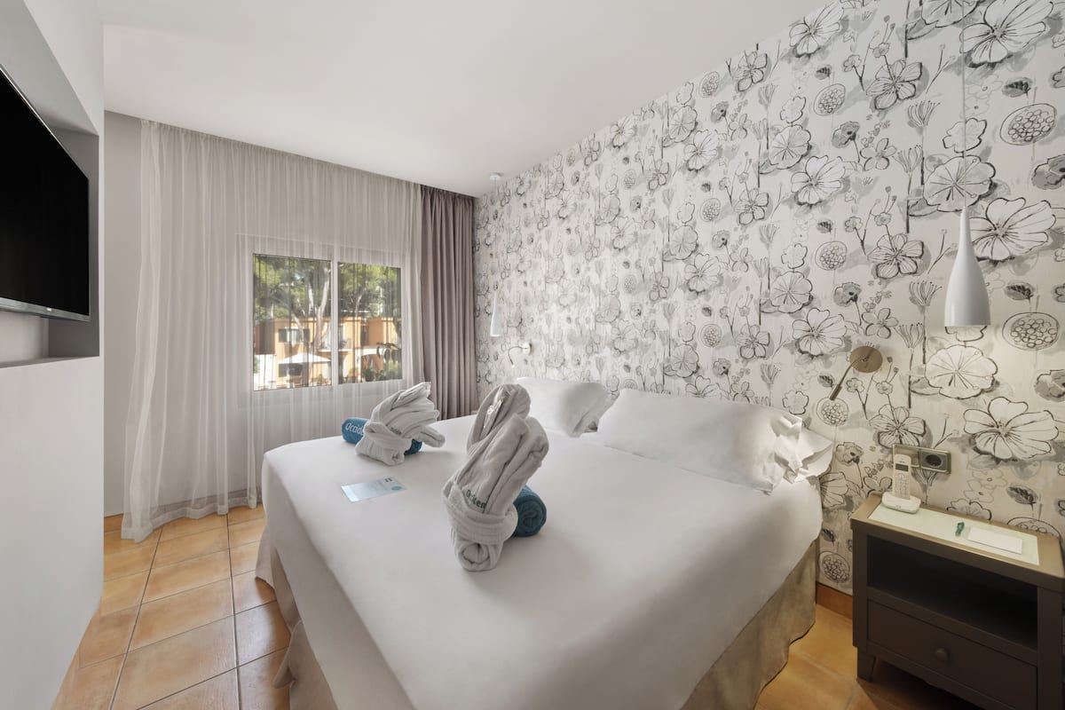 A hotel room with a bed, a nightstand, a TV, and a window with curtains.