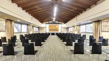 Un salón de conferencias con filas de sillas, vigas de madera en el techo y ventanas amplias.