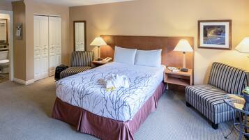 A hotel room with a large bed, two bedside tables, a striped armchair, a chair, a desk, and a wardrobe.