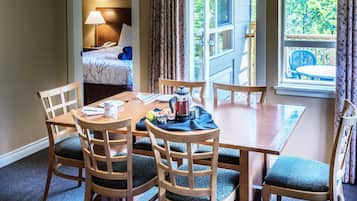 Habitación de hotel con comedor que incluye una mesa y sillas de madera, una cama con cabecera y vistas al exterior a través de una ventana.