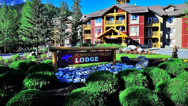 Un chalet agrémenté d’une enseigne indiquant « Pemberton Valley Lodge », entouré d’un aménagement paysager soigné et avec une chaîne de montagnes en toile de fond.