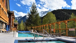 Un espace piscine agrémenté d’un panneau indiquant « Il est interdit de plonger », de chaises longues et offrant une vue sur des montagnes enneigées.