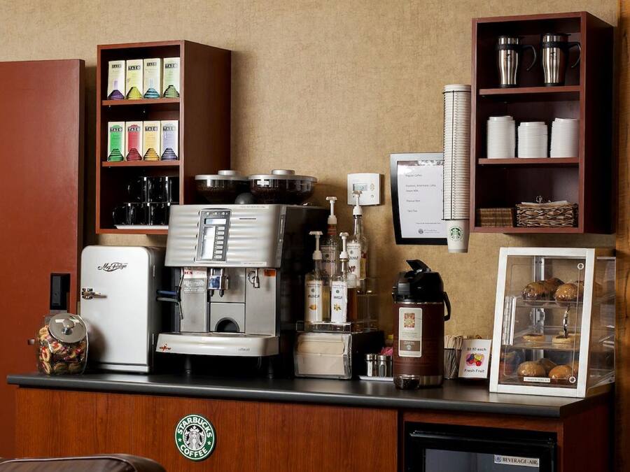 A coffee station with a coffee machine, a refrigerator, and shelves with coffee pods and cups.