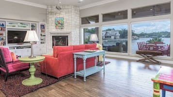 A spacious living room with a fireplace, a large window overlooking a body of water, and a cozy seating area.