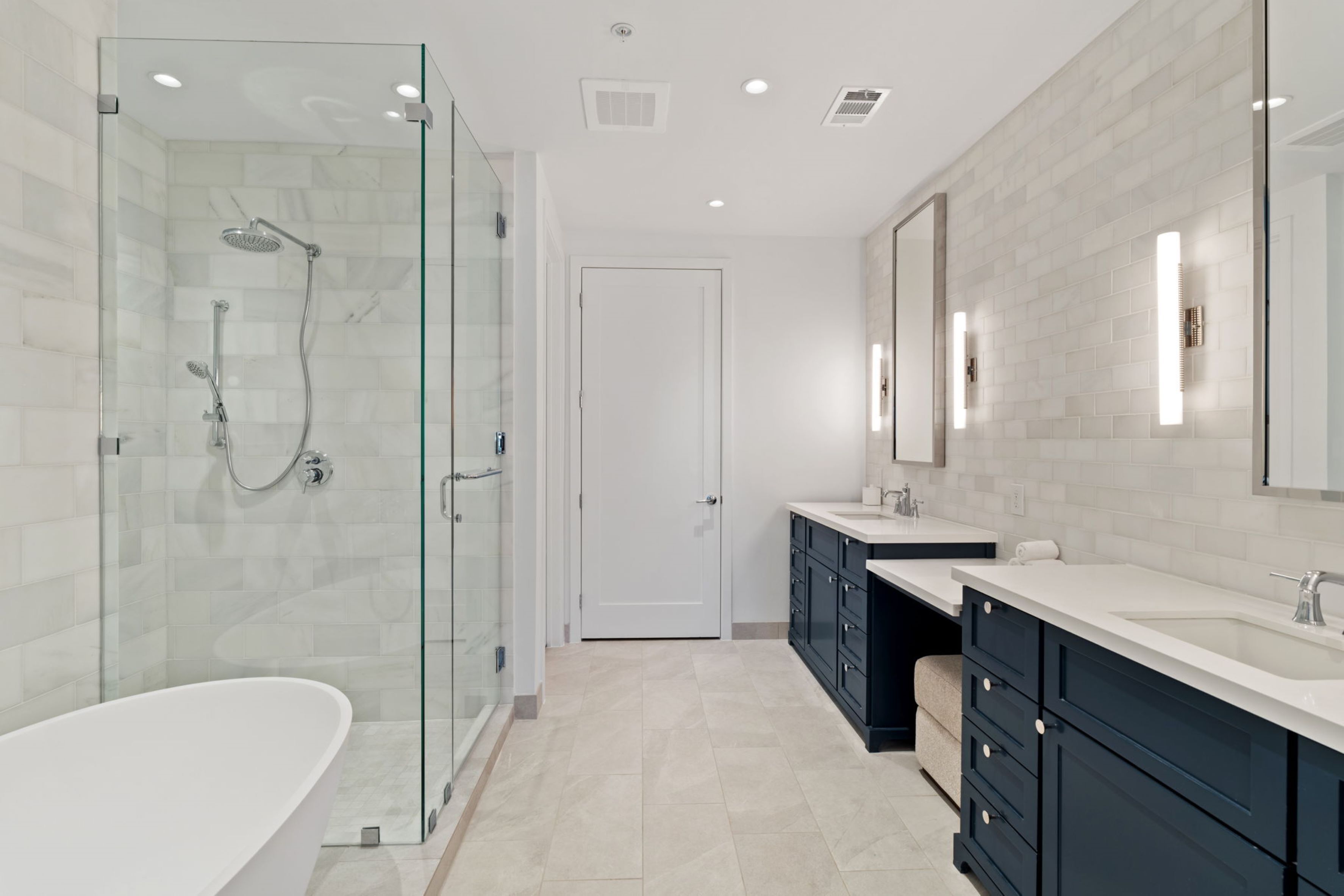 A modern bathroom with a glass-enclosed shower, a freestanding bathtub, and dark cabinetry.