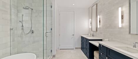 A modern bathroom with a glass-enclosed shower, a freestanding bathtub, and dark cabinetry.