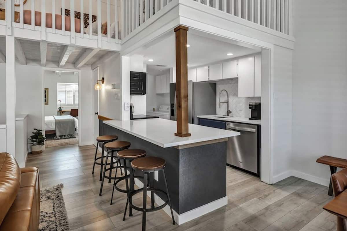 A modern kitchen with a central island, bar stools, and a dining area with a brown leather couch.