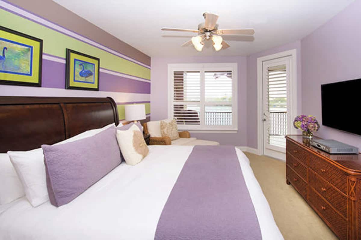 A bedroom with a bed, a dresser, a ceiling fan, a TV, and a window with blinds.