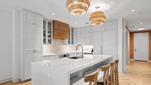 A modern kitchen with white cabinetry, a large island with bar stools, and two wicker pendant lights. - Horseshoe Bay Resort (Horseshoe Bay)