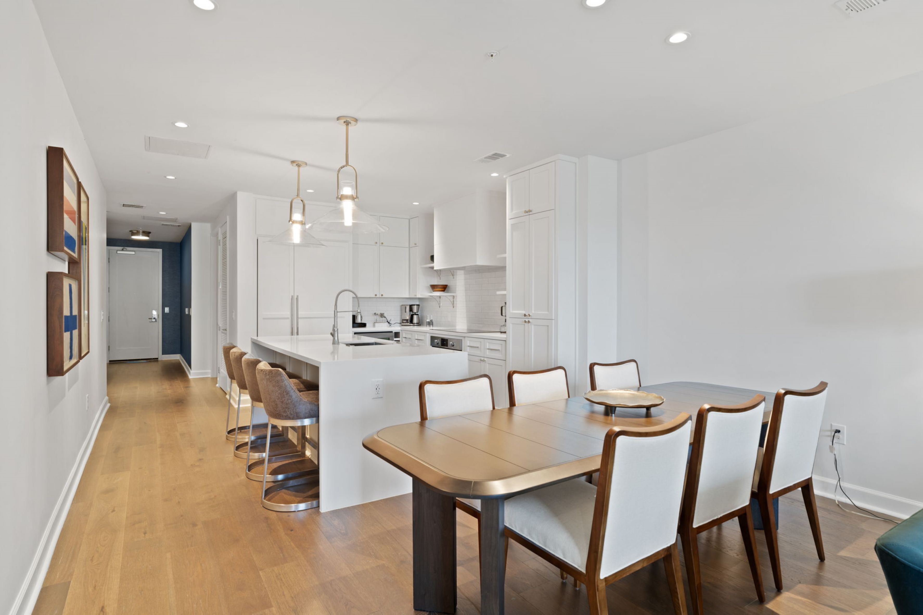 A modern kitchen with white cabinets, a central island with seating, and pendant lighting.