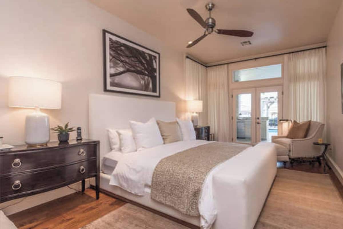 A hotel room with a large bed, a desk with a chair, a ceiling fan, and a TV on the wall.