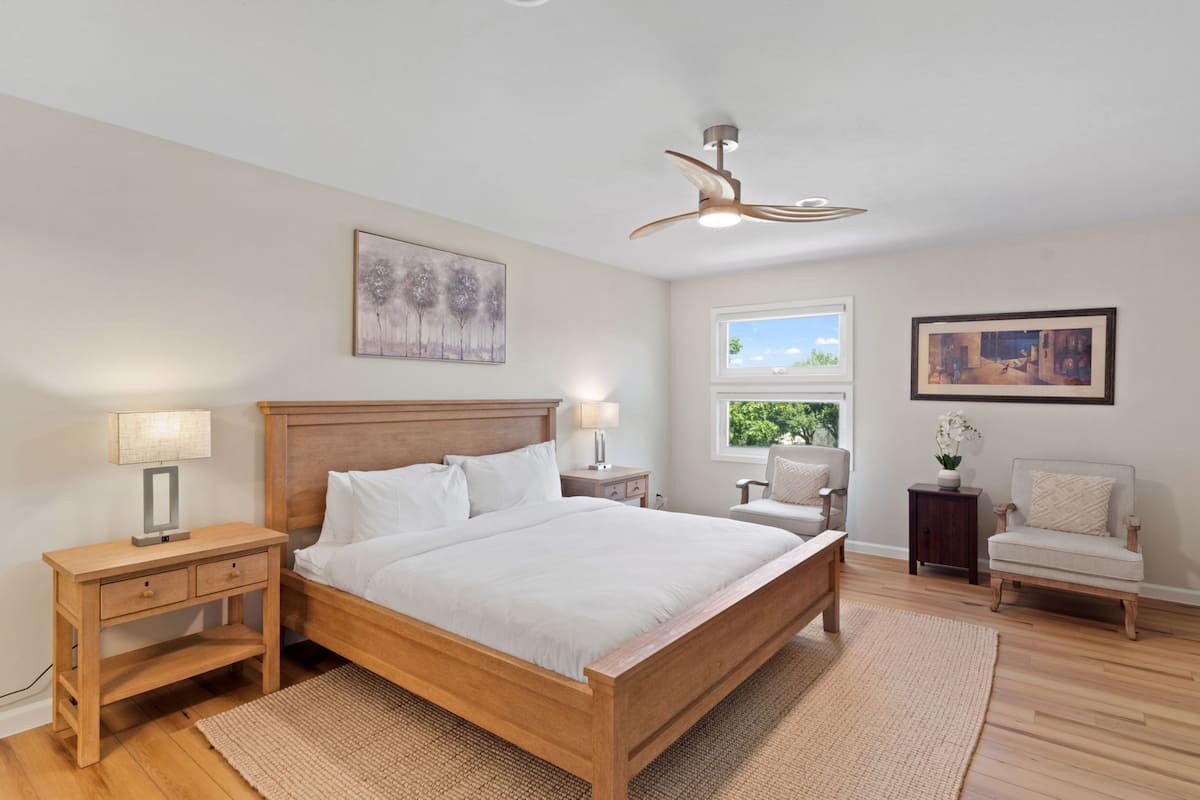 A bedroom with a wooden bed, bedside tables, a nightstand, a window with a view, and a ceiling fan.