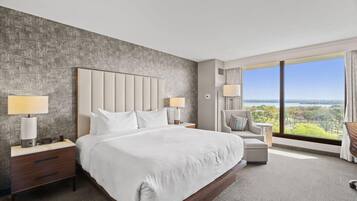 Ein modernes Hotelzimmer mit einem großen Bett, zwei Nachttischen, einem Sessel und Blick ins Freie.