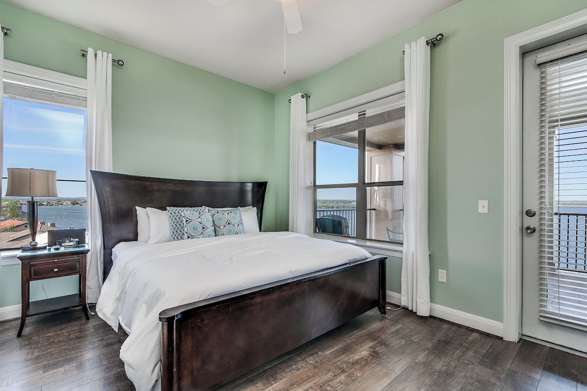A bedroom with a large bed, a nightstand, a window with a view, and a door with a window.