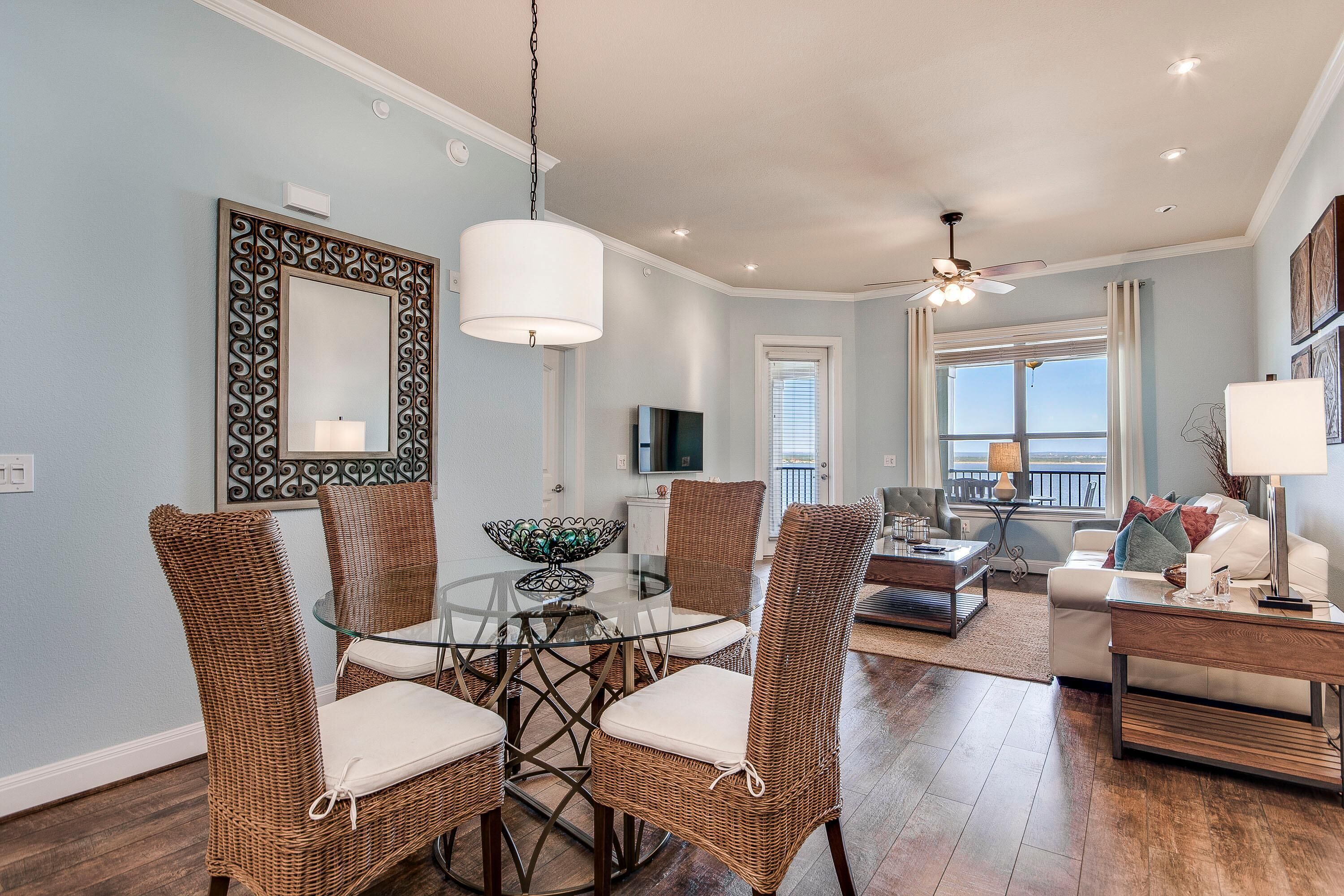 A dining area with wicker chairs, a glass table, and a ceiling fan.