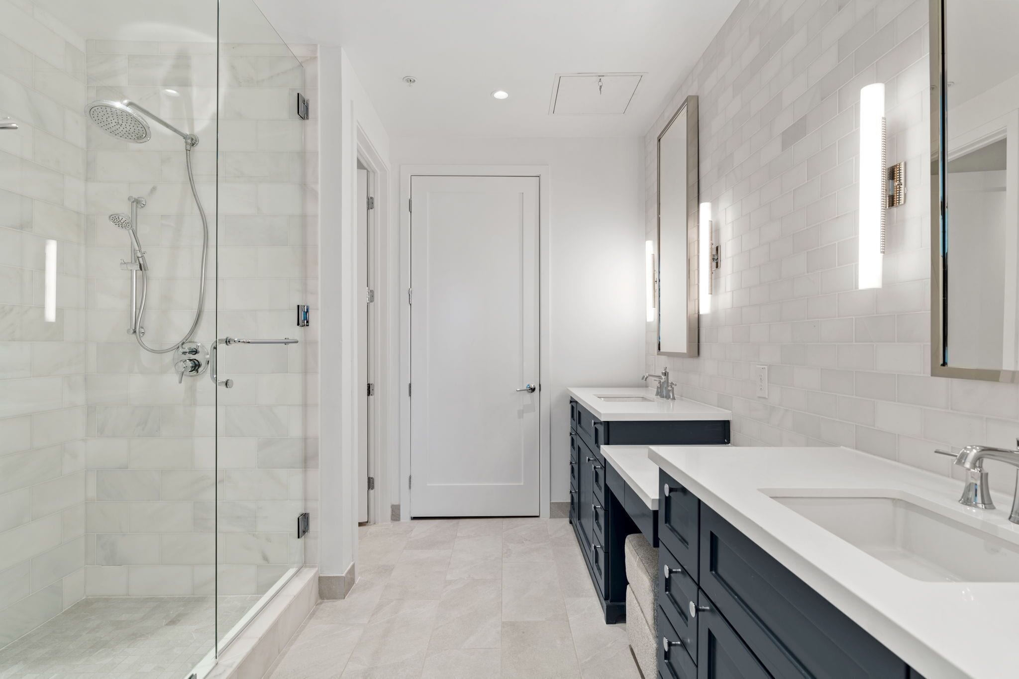 A modern bathroom with a glass shower enclosure, a white door, and a vanity with a sink and mirror.