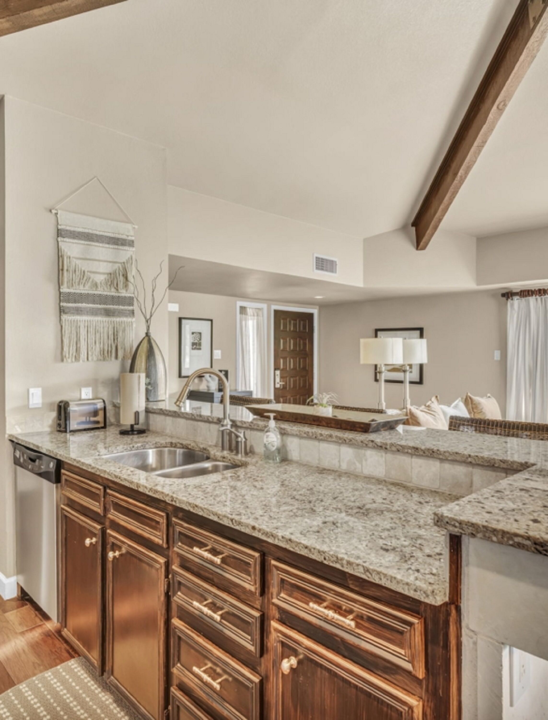 A kitchen with granite countertops, wooden cabinets, a built-in dishwasher, and a large island with a sink.