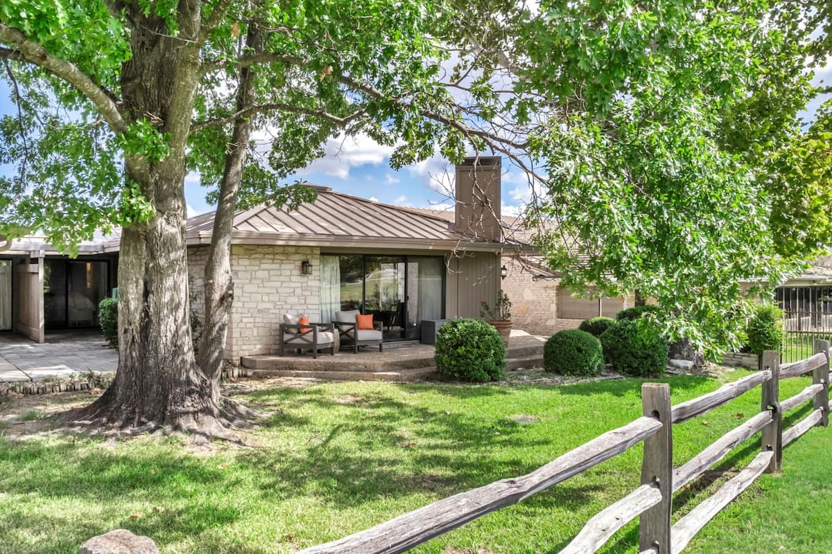 A house with a stone exterior, a covered patio, and a wooden fence.