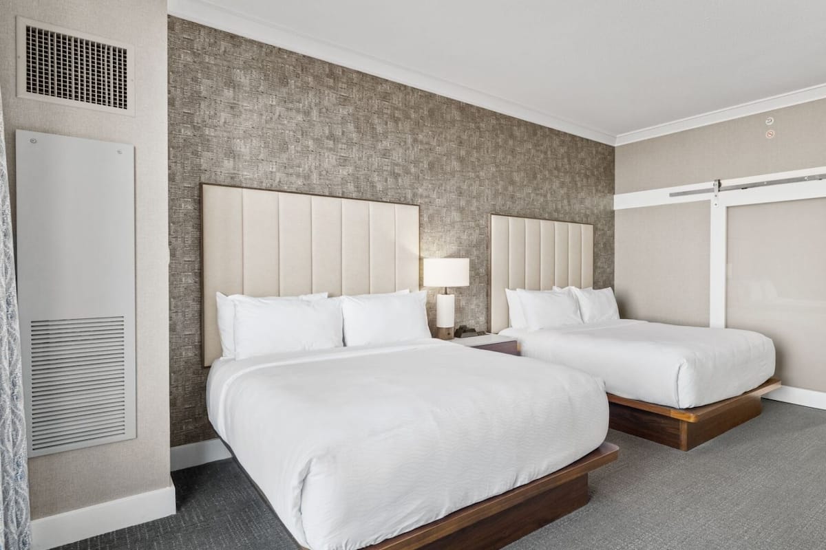 A hotel room with two beds, a large mirror, a wardrobe, and a view of the outside.