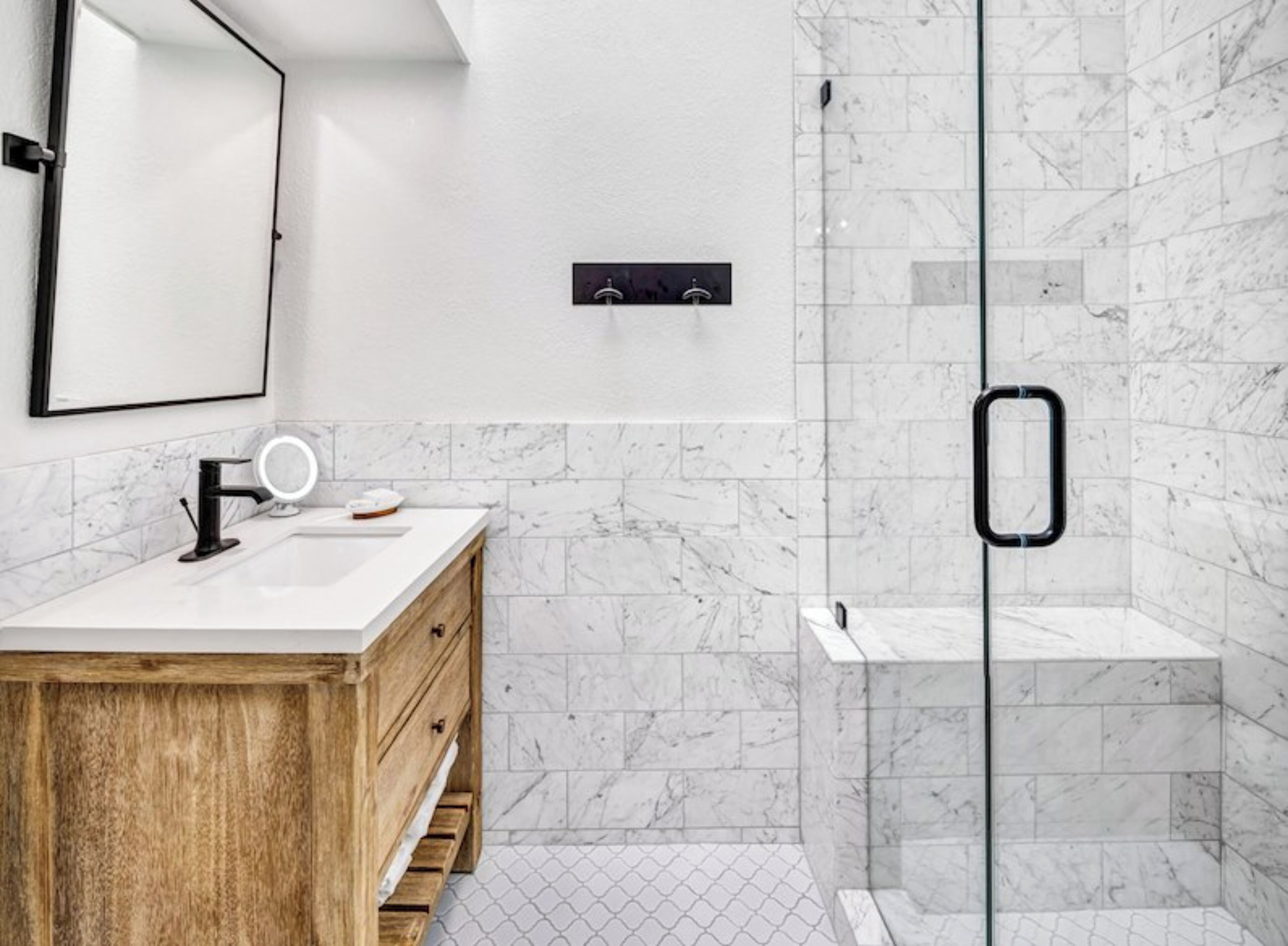 Un baño moderno con ducha de mármol, tocador de madera y un espejo grande.