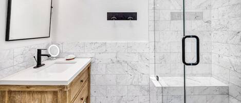 Un baño moderno con ducha de mármol, tocador de madera y un espejo grande.
