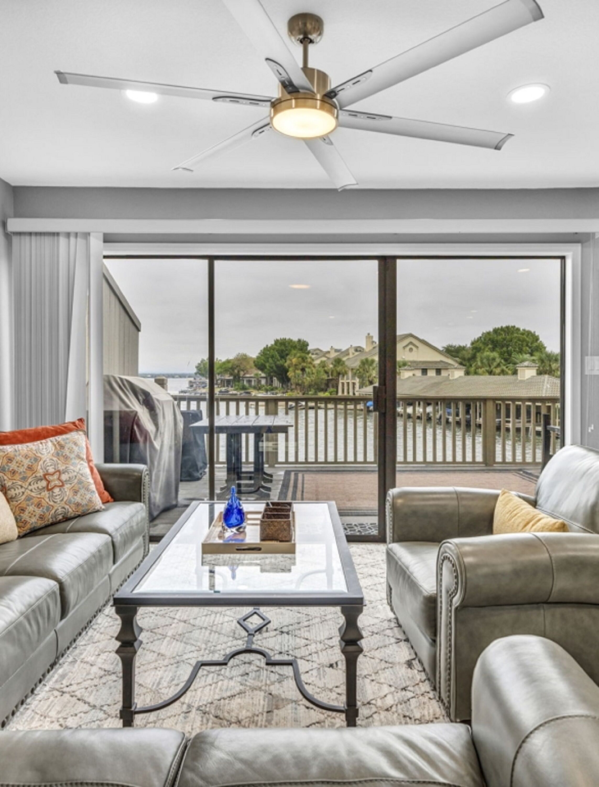 A spacious living room with a ceiling fan, a glass coffee table, and leather sofas.