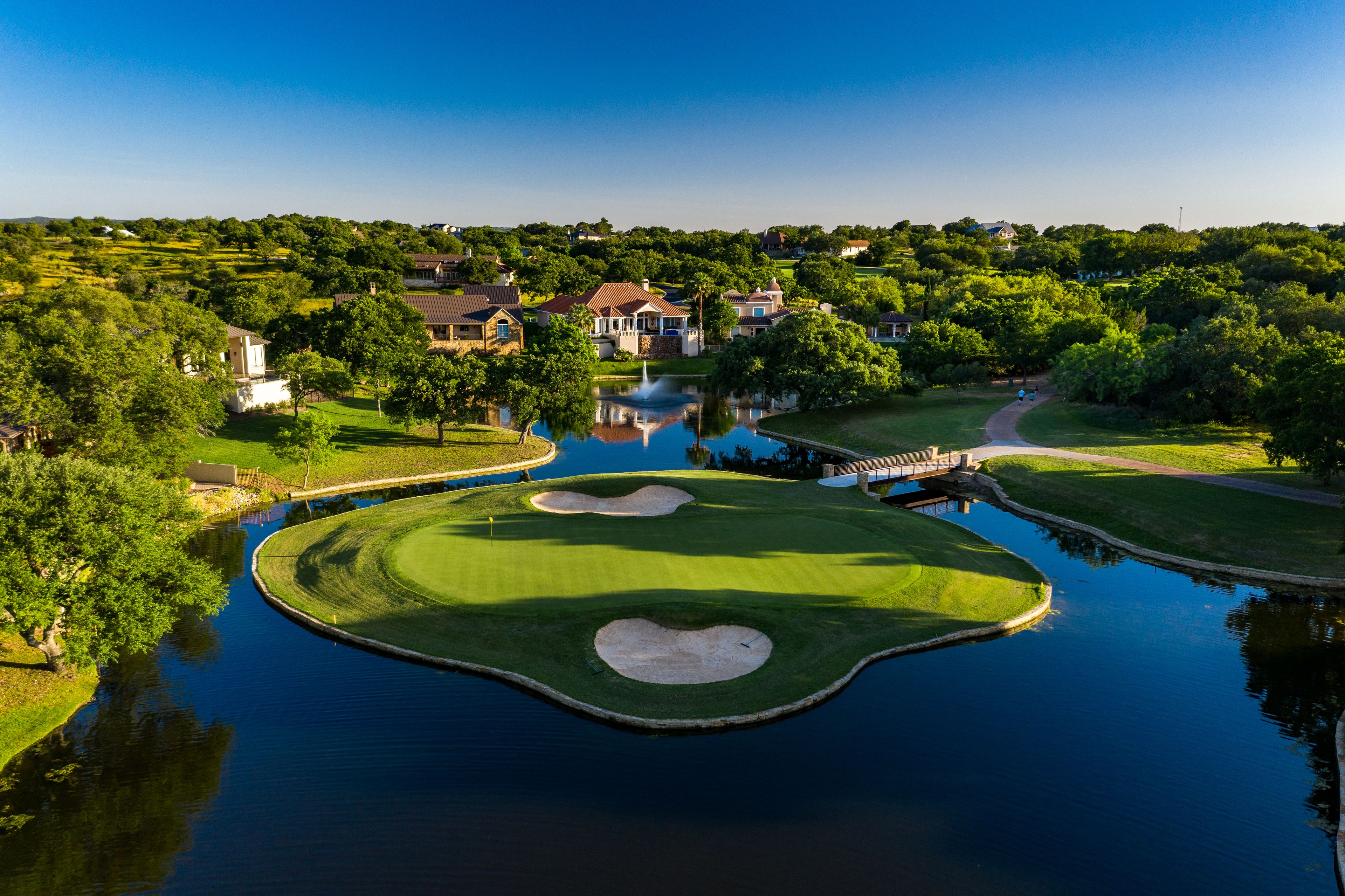 A golf course with a pond, surrounded by residential houses and lush greenery.