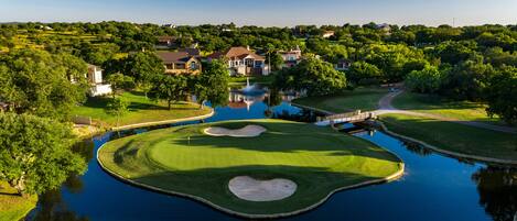 A golf course with a pond, surrounded by residential houses and lush greenery.