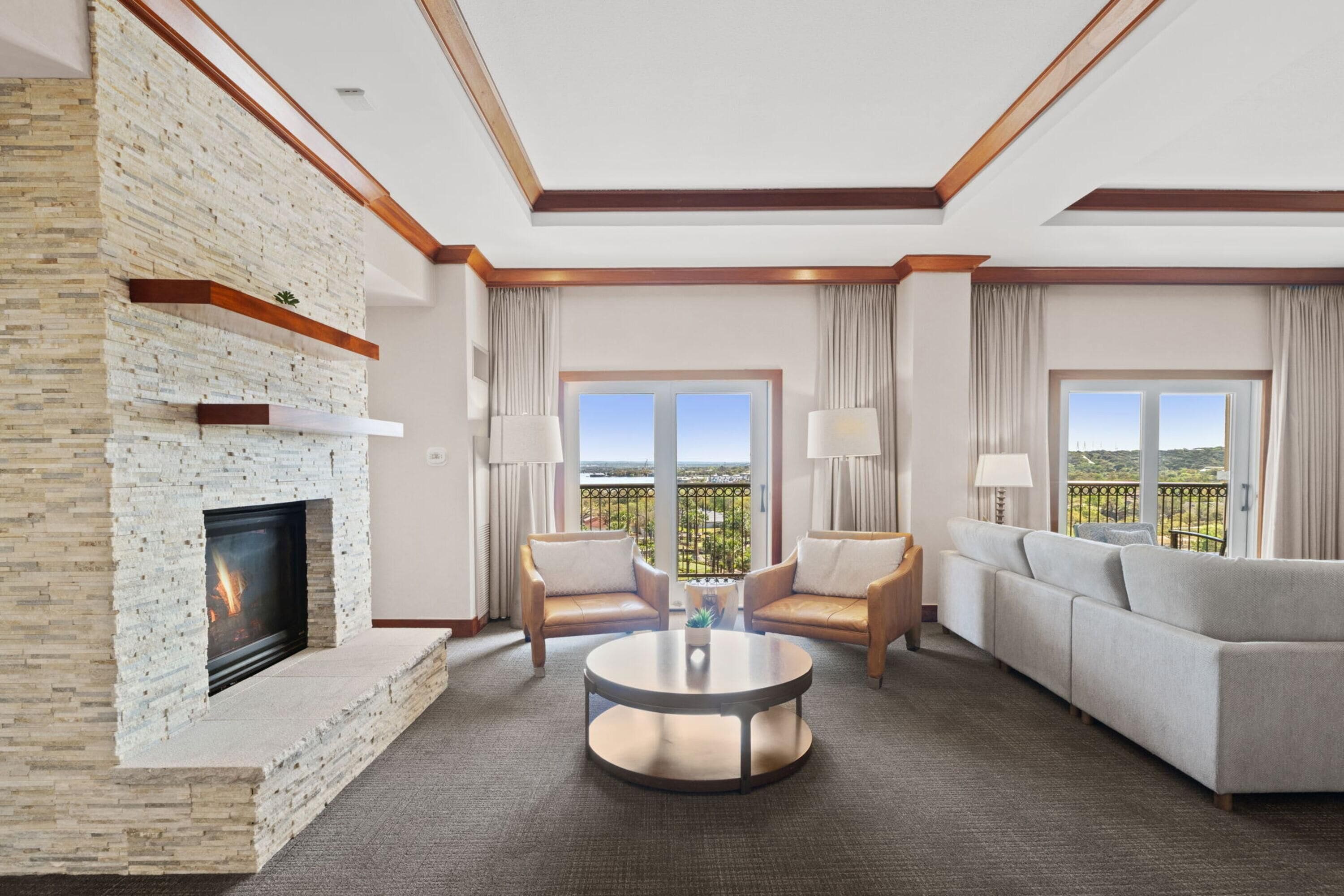 A hotel room with a fireplace, two sofas, a coffee table, and large windows with a view.