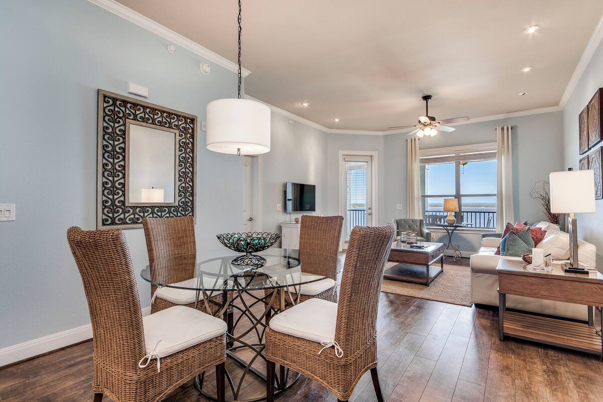 A dining area with wicker chairs and a glass table, a living room with a sofa and a TV, and a balcony with a view.