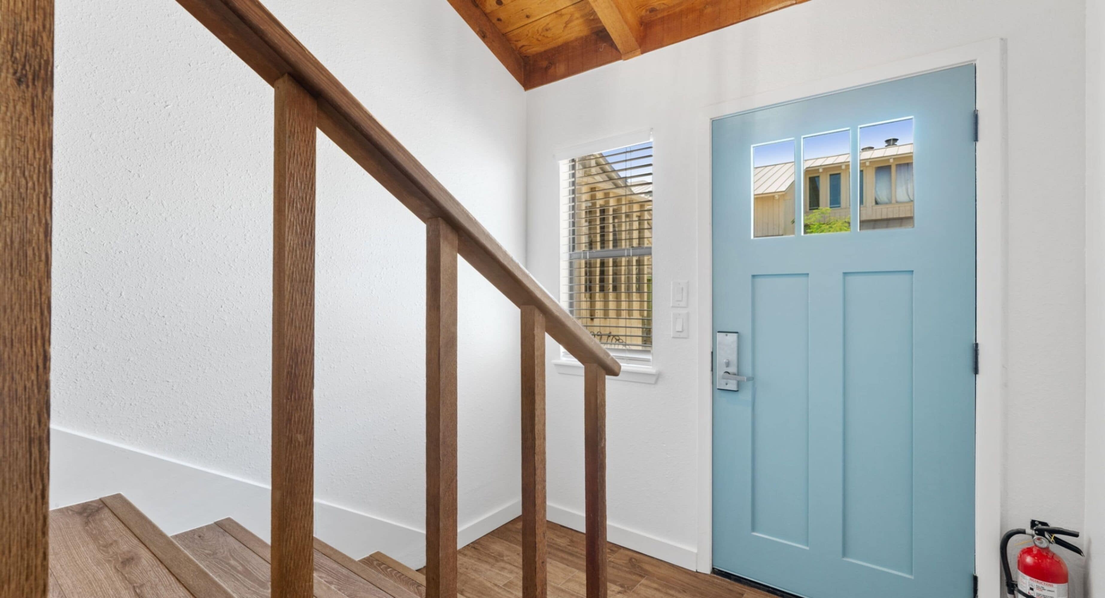 Una escalera con barandillas de madera que lleva a una puerta azul claro con un ventanal.
