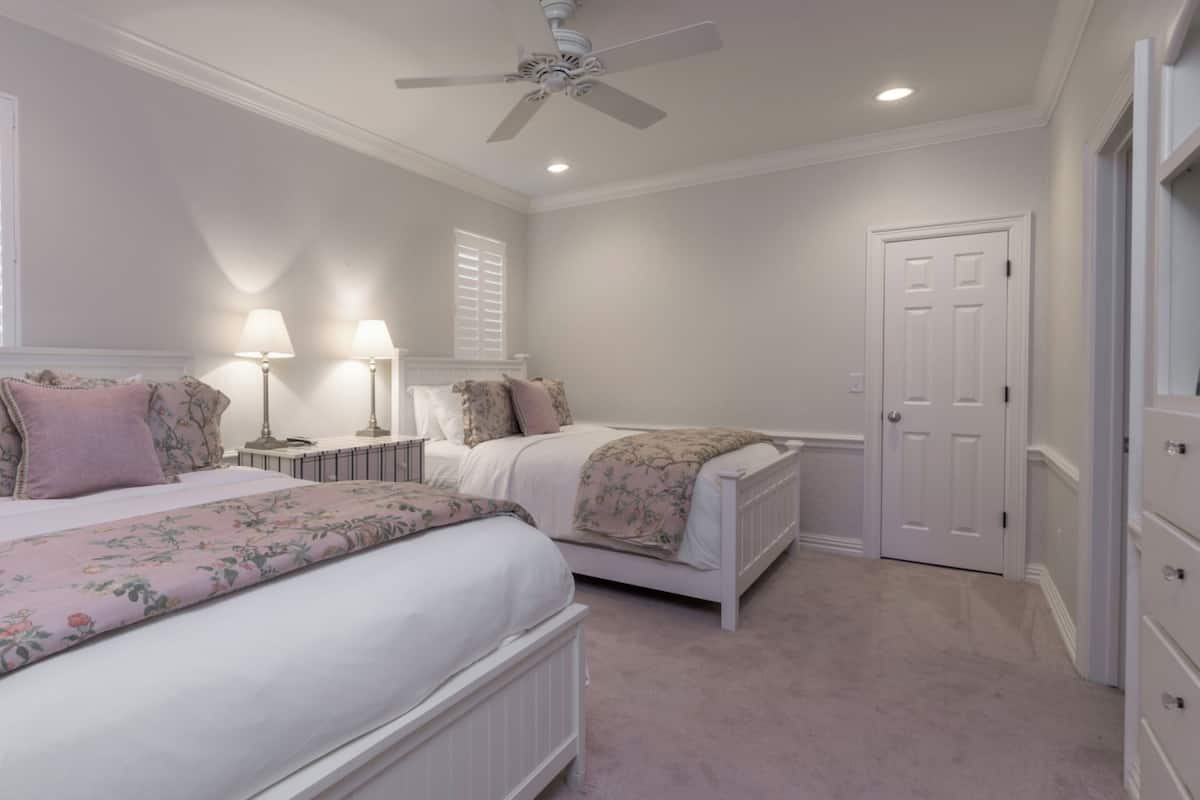 A bedroom with two beds, a ceiling fan, and a door.