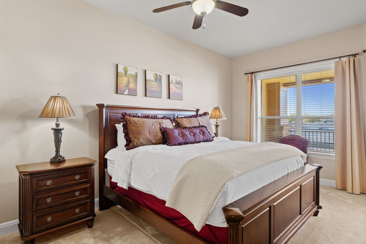 A bedroom with a wooden bed, two bedside tables, a ceiling fan, and a window with curtains.