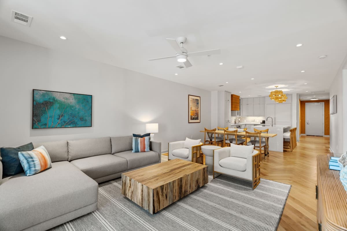 A modern living room with a gray sectional sofa, a wooden coffee table, and a dining area with a wooden table and chairs.